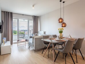 A modern dining area with a round table, grey upholstered chairs, and a vase of white flowers. - Modernes Ferienappartement in Swinemünde by Interhome (Swinoujscie)