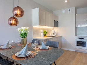 A modern kitchen with white cabinets, a built-in oven, and a dining area with a marble table set for four. - Modernes Ferienappartement in Swinemünde by Interhome (Swinoujscie)
