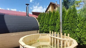 A sauna with a wooden exterior and a glass viewing area, surrounded by trees and a building with a red roof. - Wohnung mit Kamin N2 by Interhome (Zuberec)