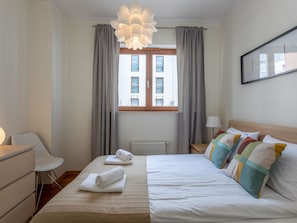 Ein Hotelzimmer mit Bett, Sessel, Schreibtisch, Heizkörper und einem fenster mit Vorhängen.