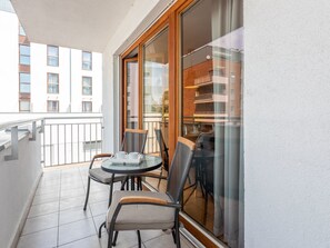 Ein Balkon mit Glastisch und Stühlen, Blick auf ein gegenüberliegendes Gebäude und einem Geländer.