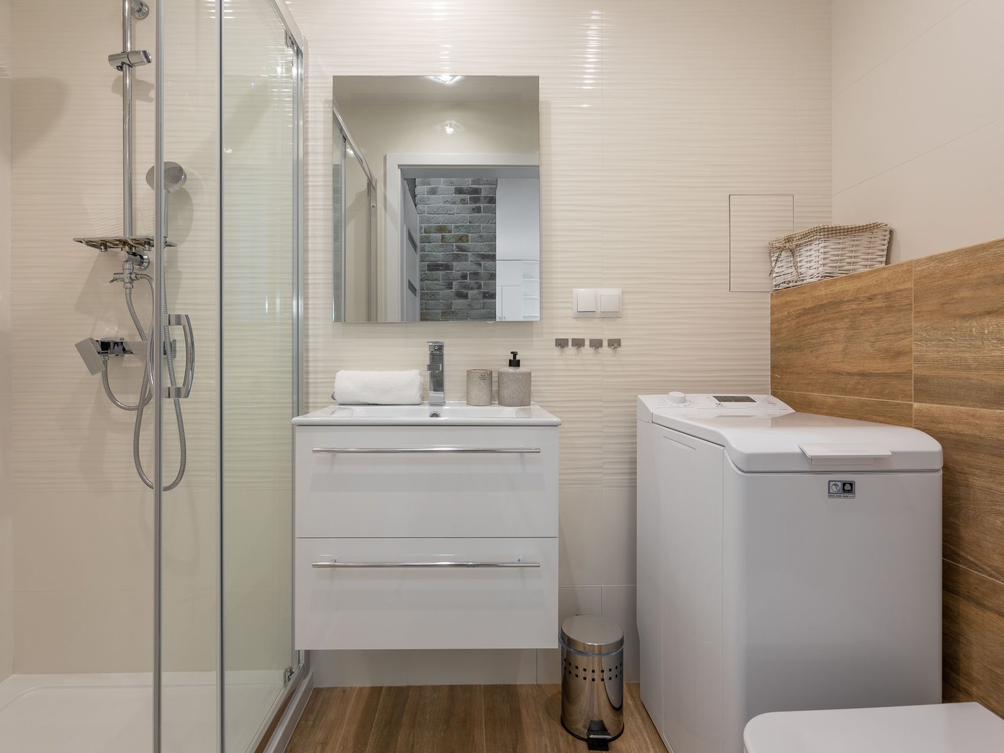 A modern bathroom with a glass shower enclosure, a white vanity with a mirror, and a wooden accent wall.