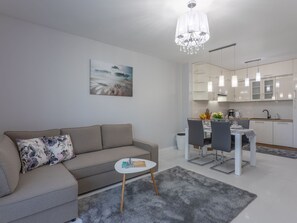 A modern living room with a sofa, a small side table, and a dining area with chairs and a table. There is a kitchen in the background with white cabinets and a chandelier. - Helle, stylische Ferienwohnung Dune 737 by Interhome (Swinoujscie)