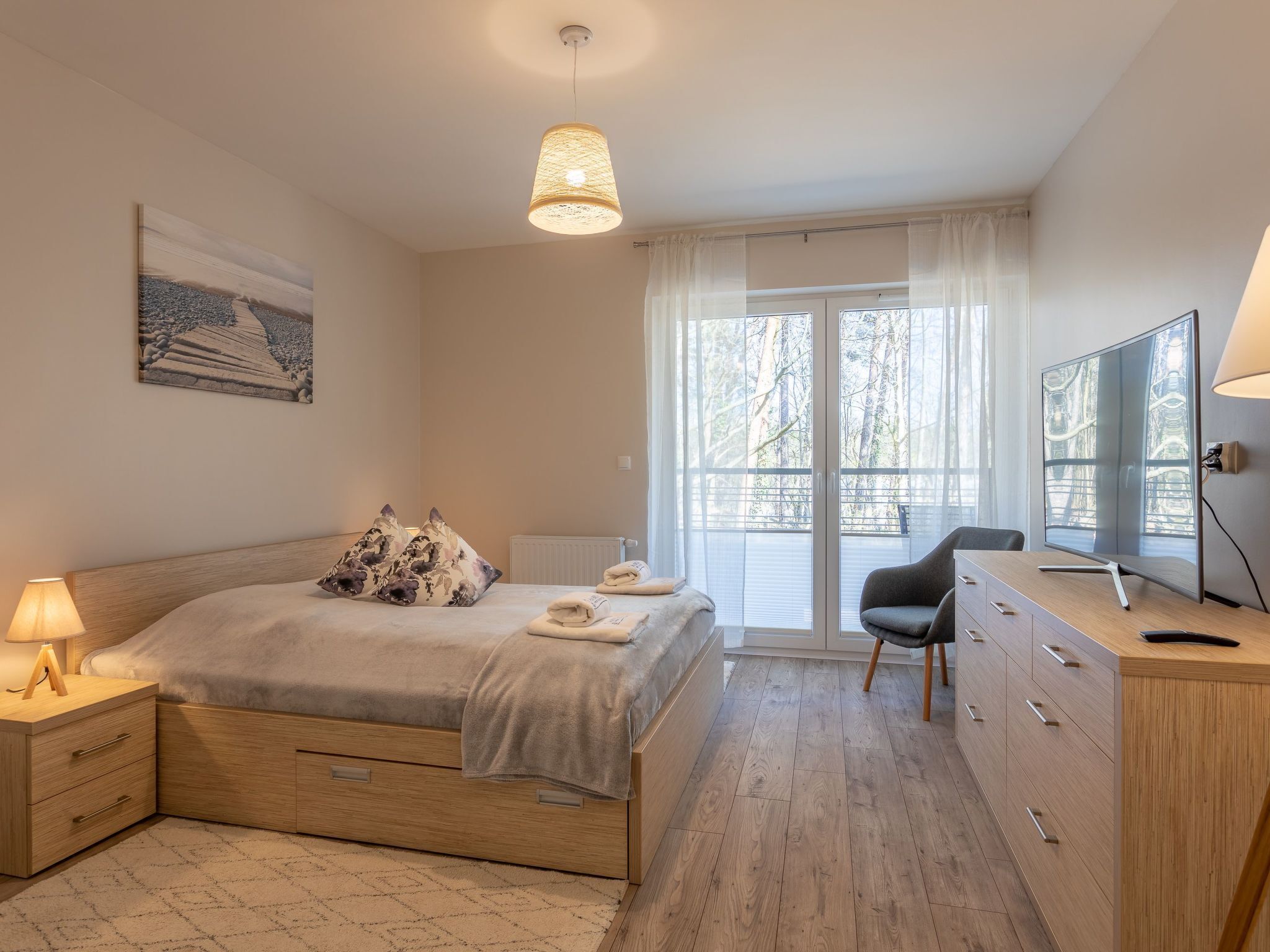 A modern bedroom with a bed, bedside lamps, a desk, and a large window with a view of trees.