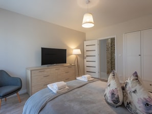 A modern bedroom with a flat-screen TV, a bedside lamp, a dresser, a bed with a grey blanket, and a floral pillow. - Helle, stylische Ferienwohnung Dune 737 by Interhome (Swinoujscie)
