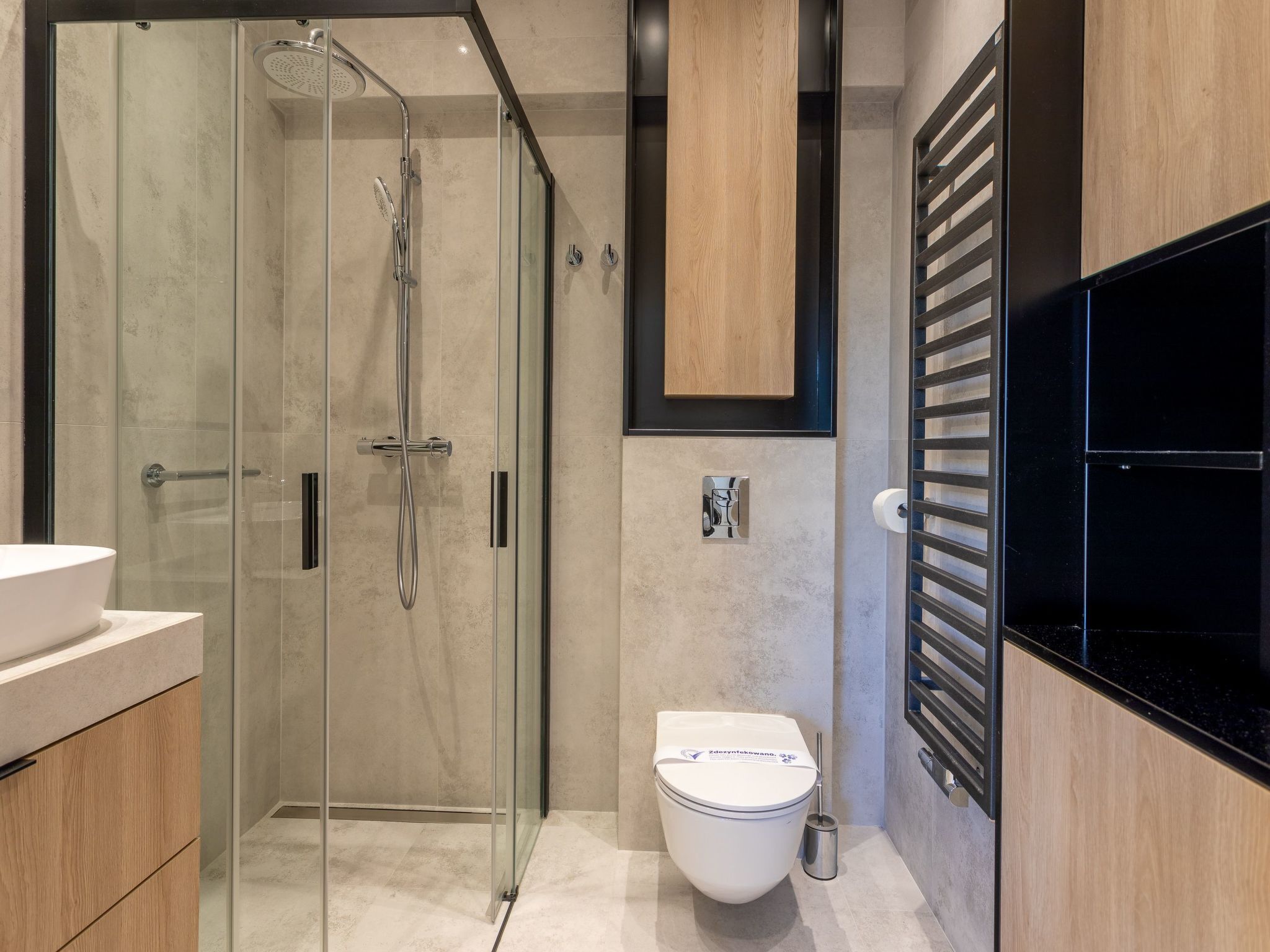 Un baño moderno con ducha de vidrio, inodoro blanco y lavamanos negro.