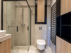 Ein modernes Badezimmer mit einer gläsernen Duschkabine, einer weißen Toilette und einem schwarzen Waschbecken.