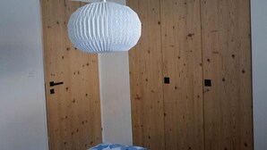 A bedroom with a wooden wardrobe, a white hanging light fixture, and a bed with a blue and white patterned bedspread. - Chesa Brünella, Wohnung Belvair by Interhome (Zuoz)