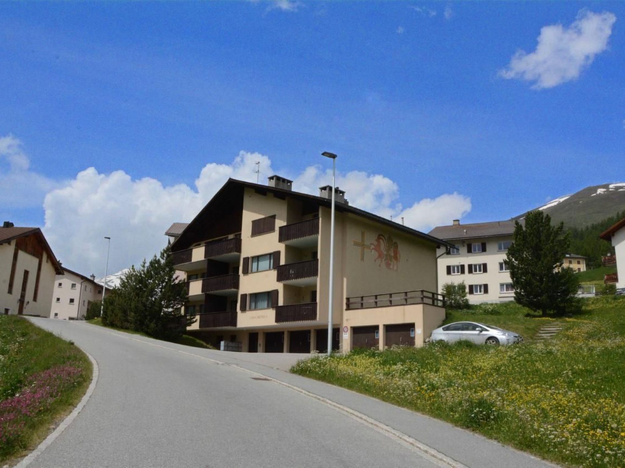 Ein mehrgeschossiges Gebäude mit Balkonen, blauem Himmel und einem geparkten Auto in der Nähe.