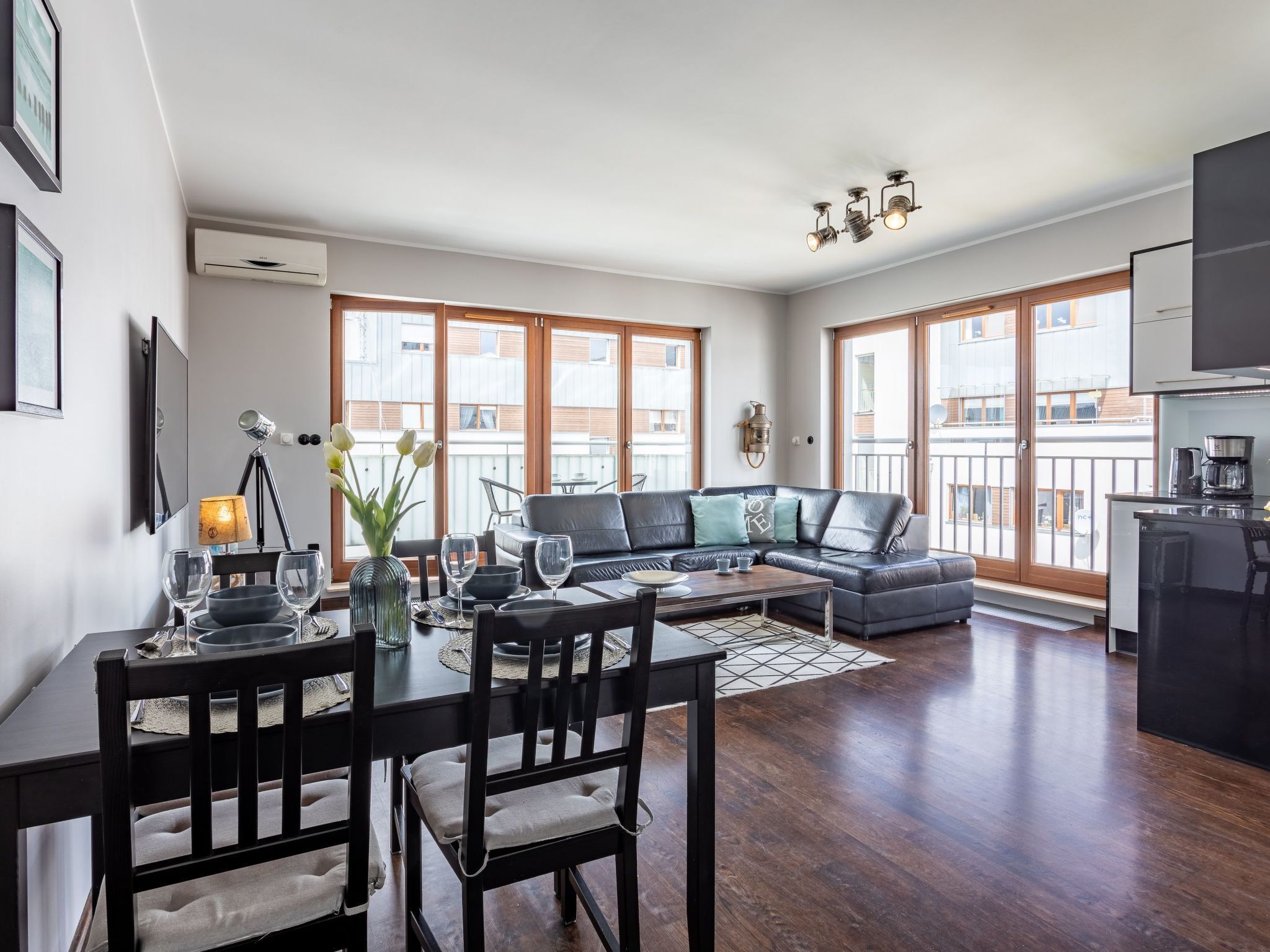 A modern living room with a dining area, large windows, a sofa, and a kitchen area.