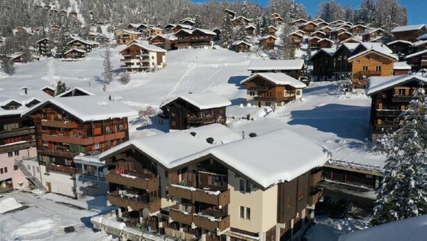 Un complejo turístico cubierto de nieve con varias construcciones tipo chalet, pistas de esquí y un cielo despejado.