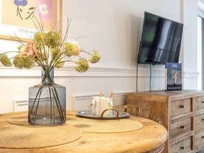 A wooden table with a clear glass vase containing flowers, a white cup with a straw, and a pair of glasses on a woven placemat. - Stilvolle Ferienwohnung Amelia in Swinemünde by Interhome (Swinoujscie)