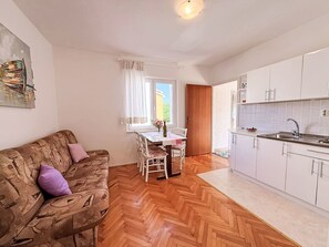 A compact living space with a sofa, dining table, chairs, a kitchen area with cabinets and a sink, and a window with curtains. - Apartment Dragica by Interhome (Polje)