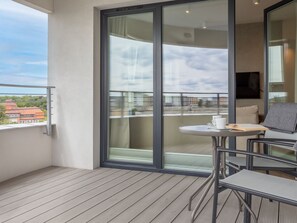 Een balkon met een houten vloer, een tafel met een stoel en uitzicht op gebouwen door een glazen deur.