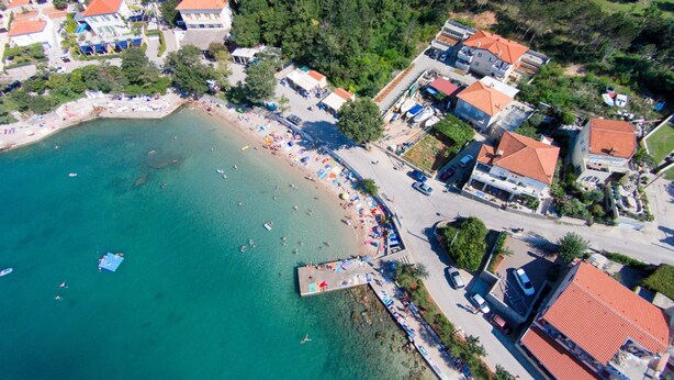 Vista aérea de uma vila costeira com praia, edifícios residenciais e um cais.