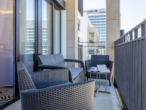A balcony with wicker furniture, a small table with a cup and book, and a view of buildings in the background. - Ferienappartement Baltic Park Fort auf Usedom by Interhome (Swinoujscie)