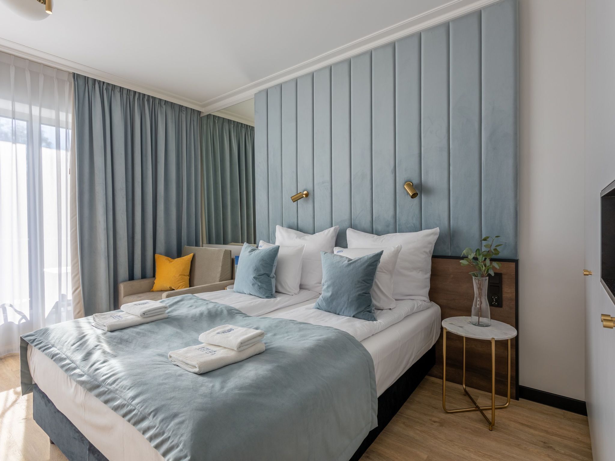 A modern hotel room with a large bed, a bedside table, and a view of the outdoors.