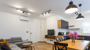 Un appartamento moderno con soggiorno, sala da pranzo e cucina. Dispone di un divano grigio, un tavolo da pranzo in legno e una cucina con forno a microonde e televisione.
