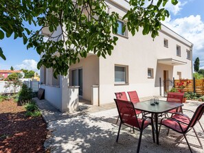 Un bâtiment moderne doté d’un patio comprenant une table et des chaises, le tout entouré de gravier et de plantes.