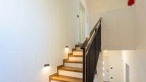 Una scala con gradini in legno e ringhiere nere, che conduce a un pianerottolo con una porta.