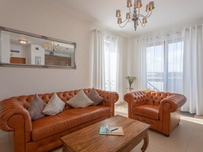 A living room with a brown leather sofa, a matching armchair, a wooden coffee table, a large mirror, and a chandelier. - Glamour direkt am Meer by Interhome (Swinoujscie)
