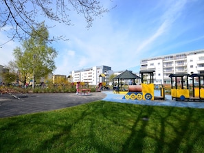 A playground with various play structures, surrounded by grass and trees, with residential buildings in the background. - Glamour direkt am Meer by Interhome (Swinoujscie)