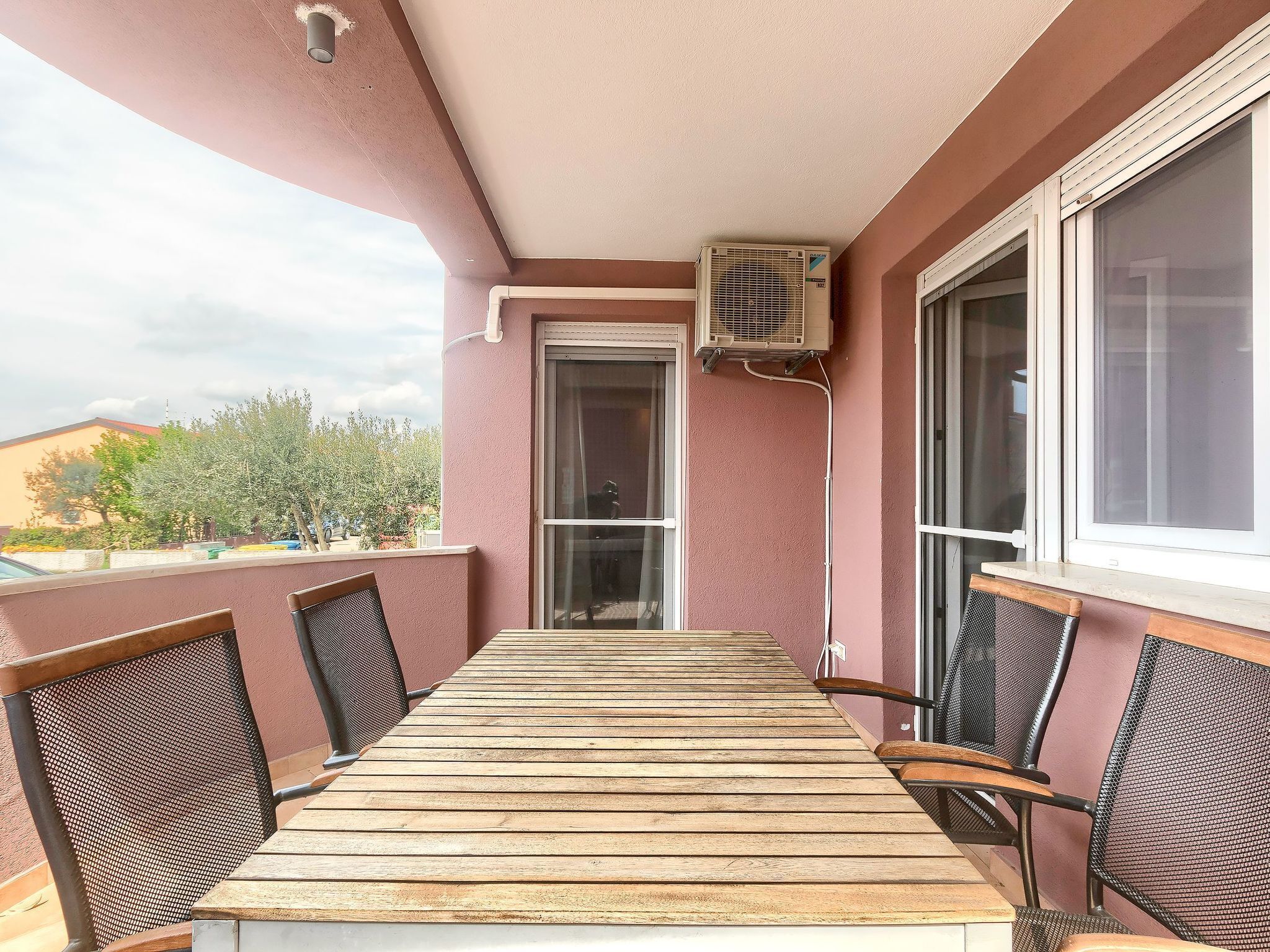 Ein Balkon mit Holztisch und -stühlen, einer Klimaanlage und Blick auf die Umgebung.