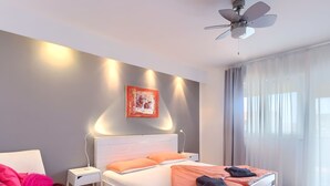 Een slaapkamer met een bed, een stoel, een nachtkastje, een plafondventilator en een raam met gordijnen.