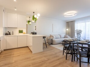 A modern kitchen with white cabinets, a central island, and hanging plants. There is a dining area with a round table, chairs, and a sofa. - White Space am Meer by Interhome (Swinoujscie)