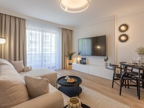 A modern living room with a sofa, a coffee table, and a dining area with chairs and a table. A flat-screen TV is mounted on the wall, and there is a potted plant on a side table. - White Space am Meer by Interhome (Swinoujscie)