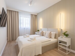 A modern hotel room with a large bed, a flat-screen TV mounted on the wall, a bedside table with a lamp, and a small plant on a nightstand. - White Space am Meer by Interhome (Swinoujscie)