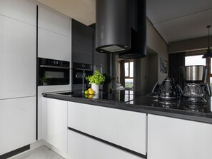 A modern kitchen with a black countertop, white cabinets, a black range hood, a coffee maker, and a view of the outdoors. - "Platan Tower 113" by Interhome (Swinoujscie)