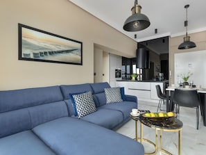A modern living room with a blue sofa, a dining area with a table set for two, and a kitchen in the background. - "Platan Tower 113" by Interhome (Swinoujscie)