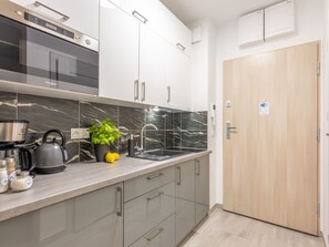 A modern kitchen with a built-in oven, a kettle, and a sink. There is a wooden door and a sign indicating Wi-Fi availability. - Strandnahe, gemütliche Ferienwohnung in Swinemünde by Interhome (Swinoujscie)