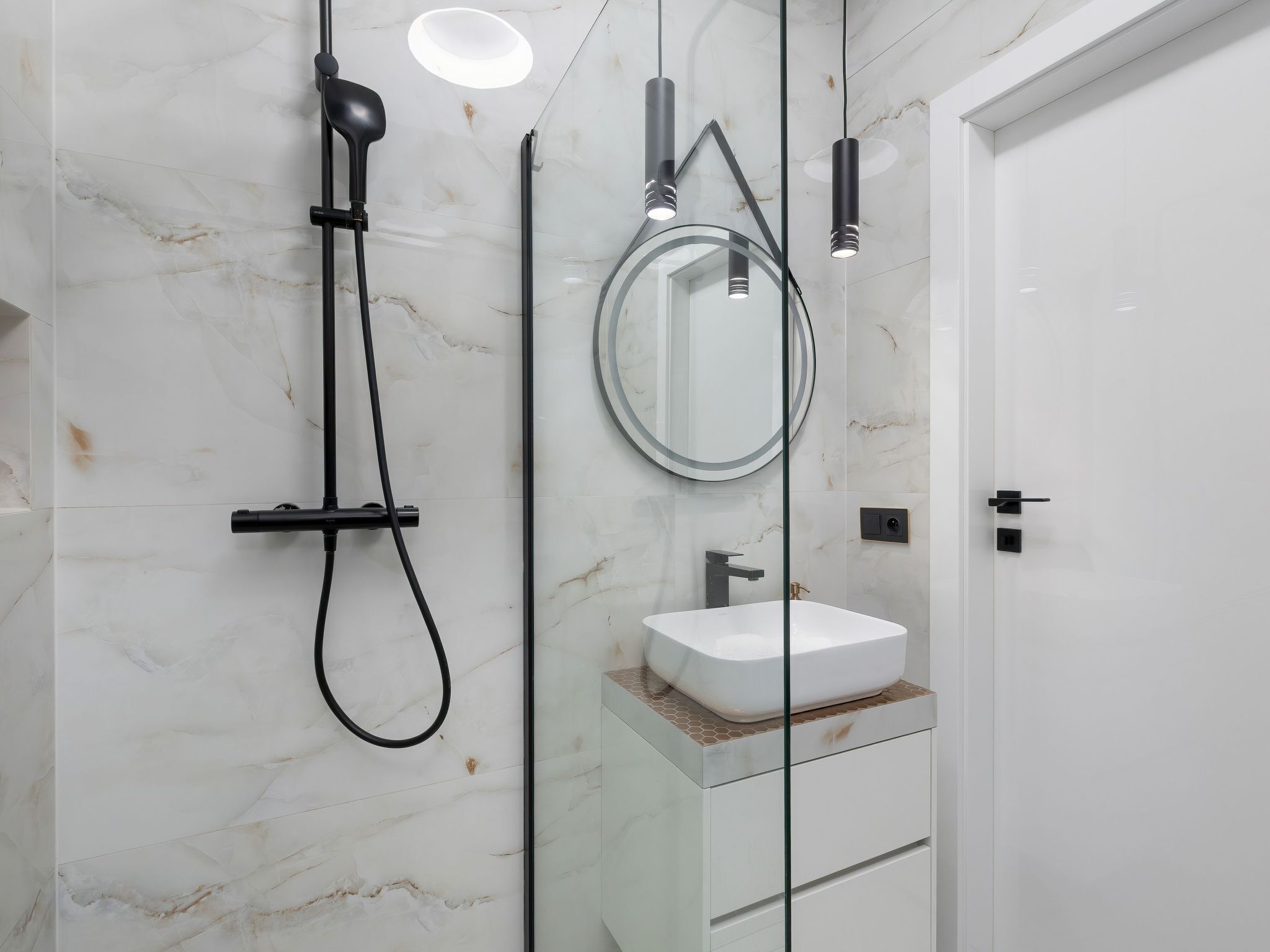 A modern bathroom with a white marble wall, a glass-enclosed sink, and a handheld showerhead.