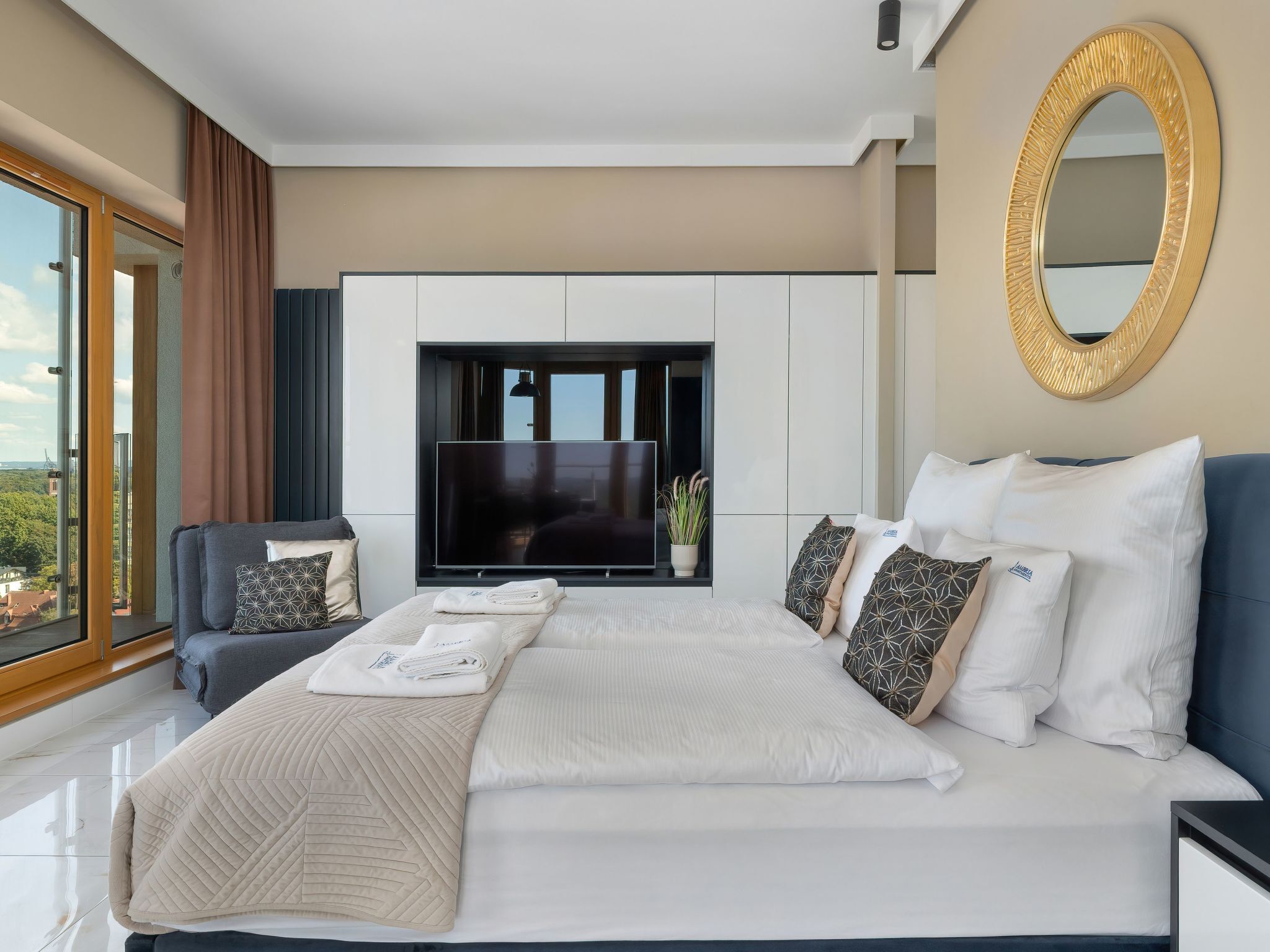 Ein modernes Schlafzimmer mit einem großen Bett, einem Flachbildfernseher und Blick ins Freie.