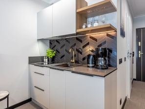 Eine moderne Küche mit weißen Schränken, einer schwarzen Arbeitsplatte, einer Kaffeemaschine und einer Pflanze.