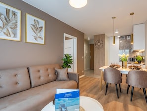 A modern living room with a beige sofa, a dining area with a white table and chairs, and a kitchen in the background. - Stilvoll eingerichtete Ferienwohnung am Meer by Interhome (Swinoujscie)