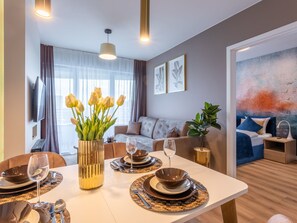 A modern living room with a sofa, a dining table set with plates and glasses, and a large window with curtains. - Stilvoll eingerichtete Ferienwohnung am Meer by Interhome (Swinoujscie)