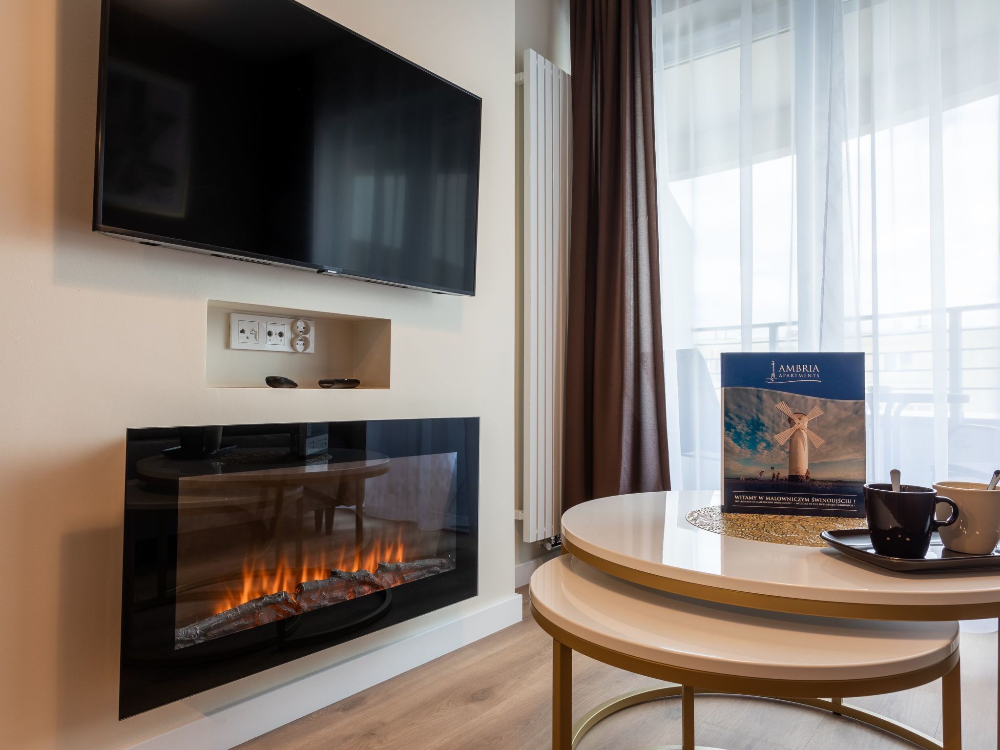 Una sala de estar moderna con un televisor de pantalla plana en la pared, una chimenea con fuego a la vista, una mesa redonda con una bandeja y un folleto sobre la mesa.