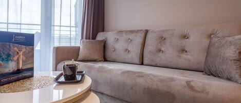 Ein Wohnzimmer mit einem beigefarbenen Sofa, einem runden Couchtisch und zwei gerahmten Blätterbildern an der Wand.