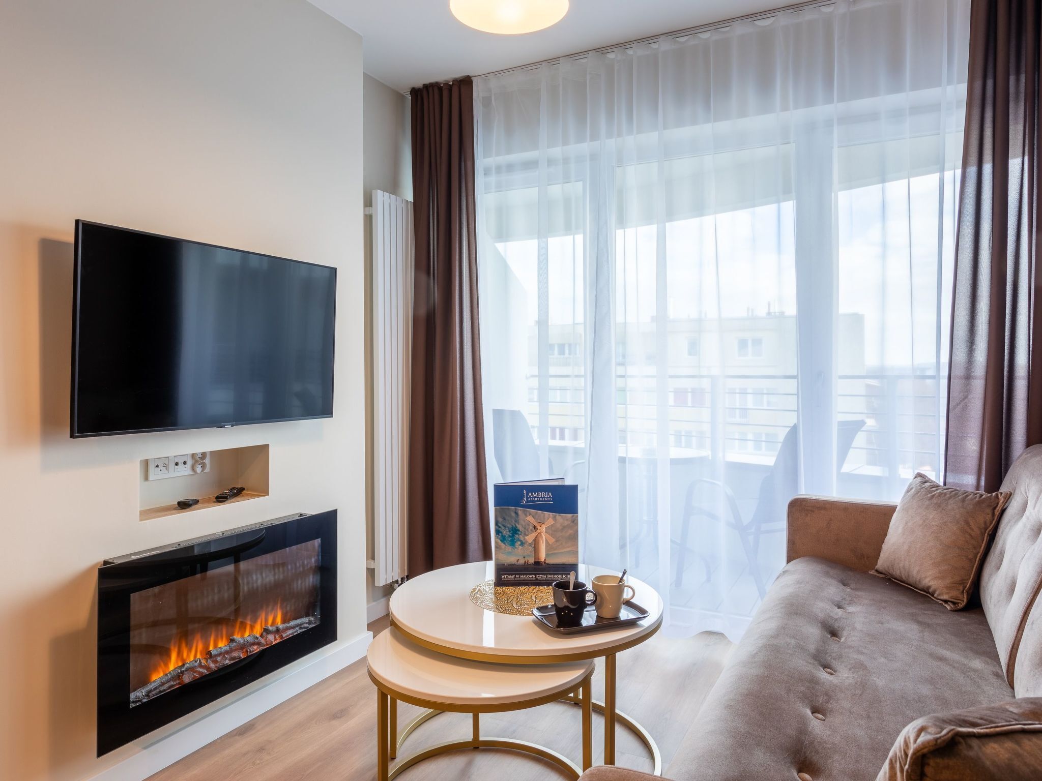 A modern living room with a flat-screen TV, a fireplace, a round coffee table, and a sofa.