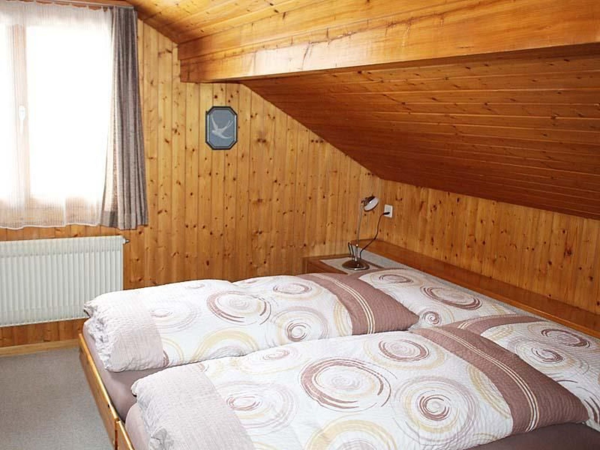 Ein Zimmer mit Holzwänden, einem Bett, einem Fenster mit Vorhängen und einer Wandleuchte.