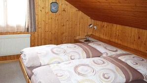 Een kamer met houten lambrisering, een bed, een raam met gordijnen en een wandlamp.