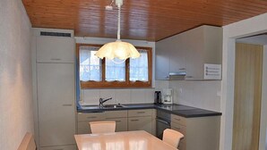Een kleine keuken met een eethoek, houten plafond en een raam met gordijnen.