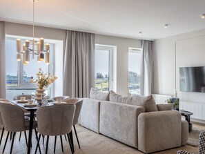 Ein modernes Wohnzimmer mit einer Eckcouch, einem Esstisch, Stühlen und einem an der Wand montierten Fernseher.