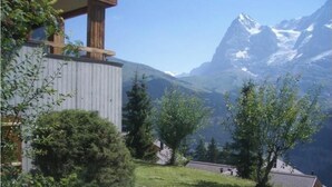 Una cabaña de montaña con terraza de madera y vistas a picos nevados.
