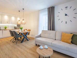 A modern living room with a sofa, a dining table with chairs, and a kitchen area with cabinets and a window. - Ferienappartement Matejki direkt an der Promenade by Interhome (Swinoujscie)