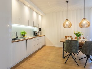 A modern kitchen with white cabinets, a wooden countertop, and a dining area with a table and chairs. - Ferienappartement Matejki direkt an der Promenade by Interhome (Swinoujscie)