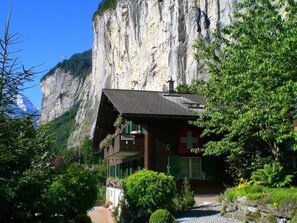 Una cabaña de montaña con un techo pronunciado, una bandera suiza y vistas a un acantilado rocoso.